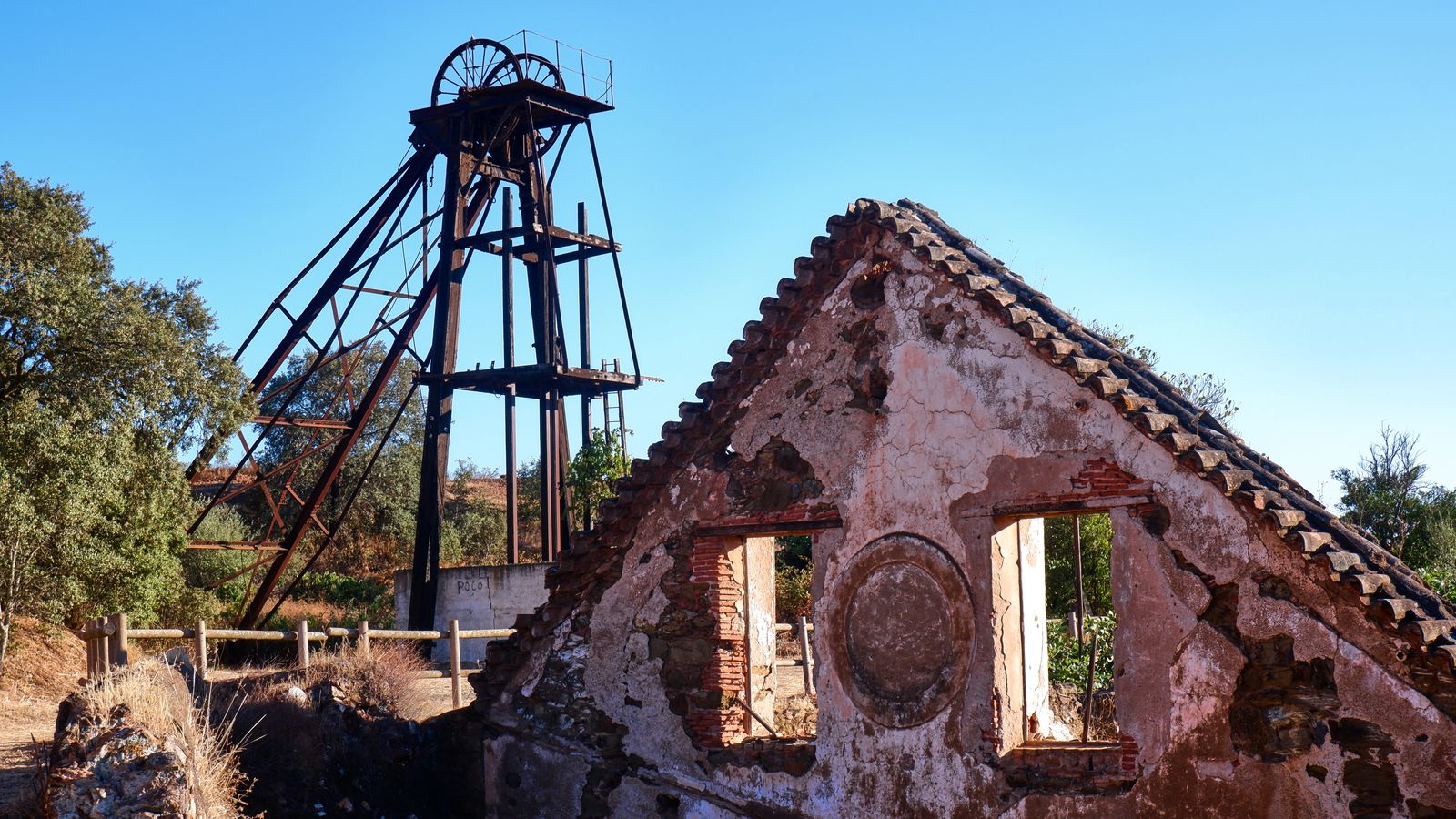 A decaying mine headframe and collapsing timber buildings on bare ground
